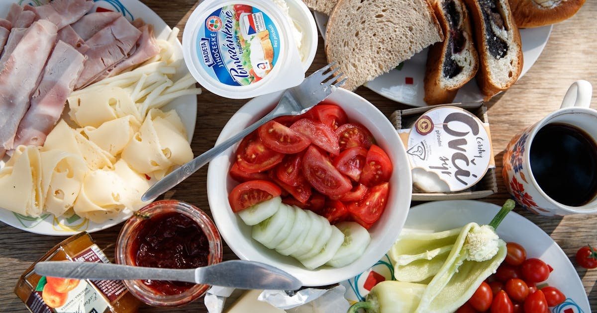 Delicious breakfast setup with cheese, cold cuts, bread, and fresh vegetables.