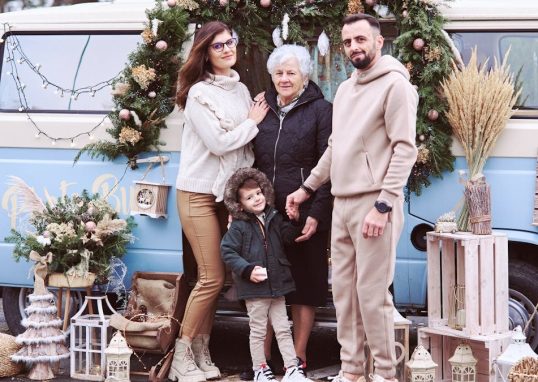 A multi-generational family posing with festive Christmas decorations outside a decorated van.